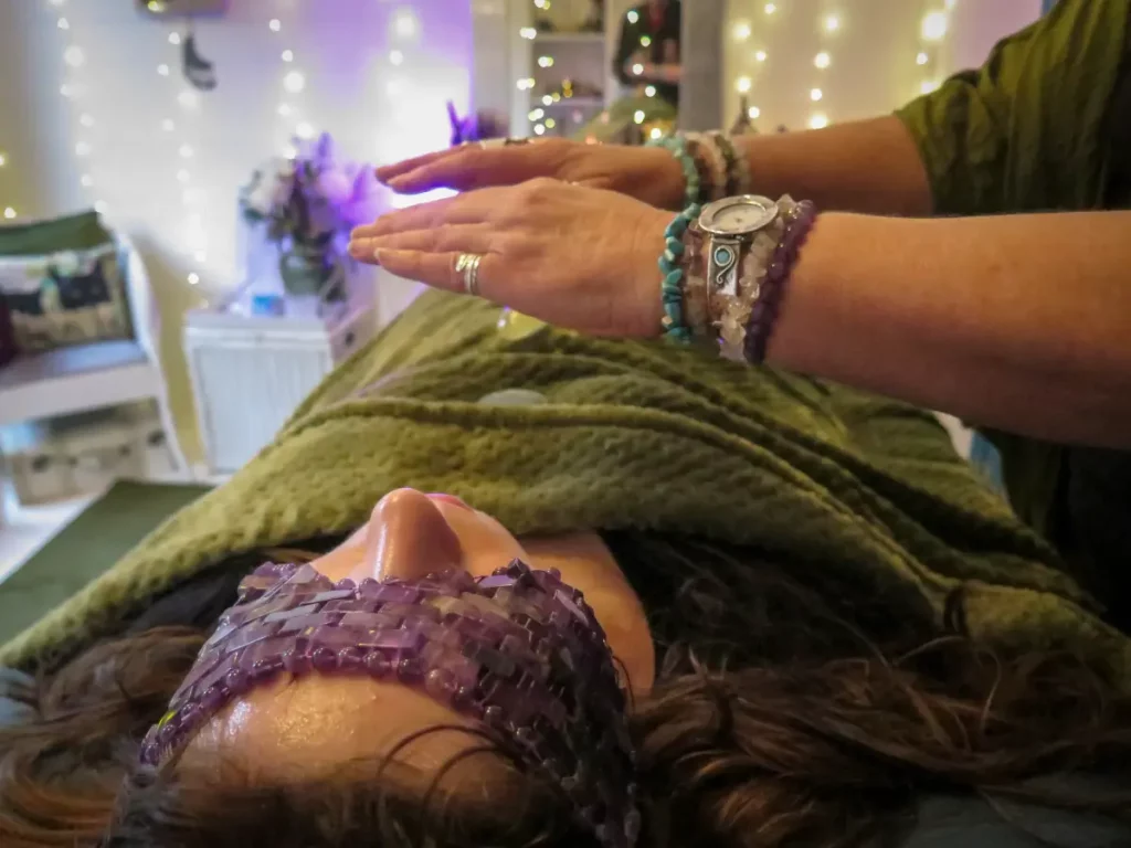 Reiki Master in Maidenhead Berkshire giving Reiki Healing to a client laying on a treatment couch covered in a green blanket with crystals on her body. The Reiki master is hovering her hands over the client.