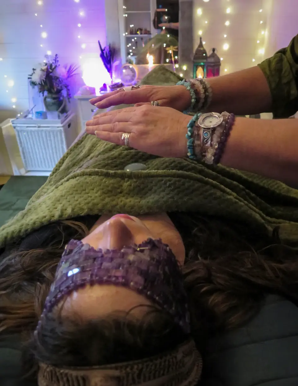 Immerse in Nature & Wellbeing: Reiki Forest Bath Experience, now. Reiki Master in Maidenhead Berkshire giving Reiki Healing to a client laying on a treatment couch covered in a green blanket with crystals on her body. The Reiki master is hovering her hands over the client.