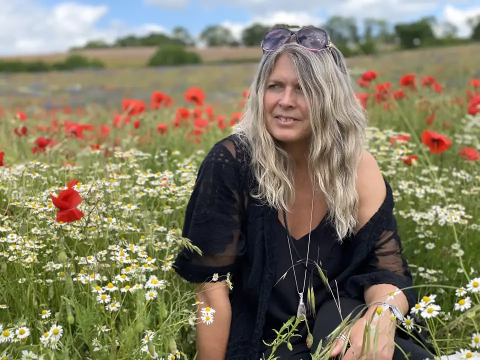 Sarah from From Dragon to Dragonfly Reiki Master sitting in a field of poppies on a sunny day